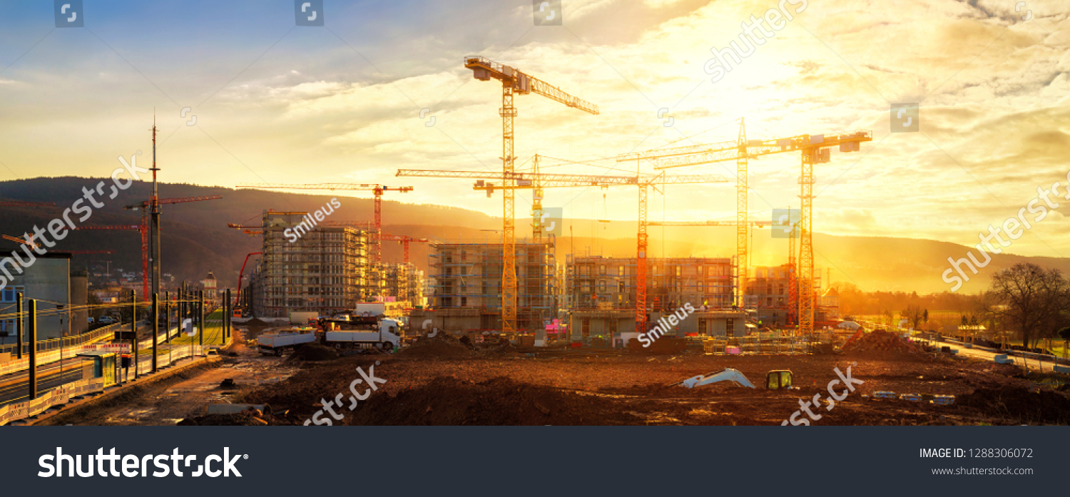 Large construction site including several cranes working on a building complex, illumined by warm gold sunlight #1288306072