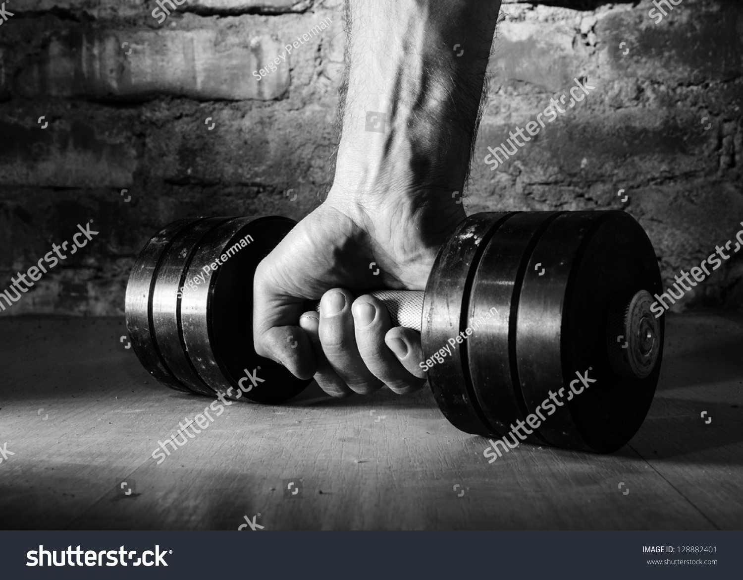 male hand is holding metal barbell against brick wall #128882401