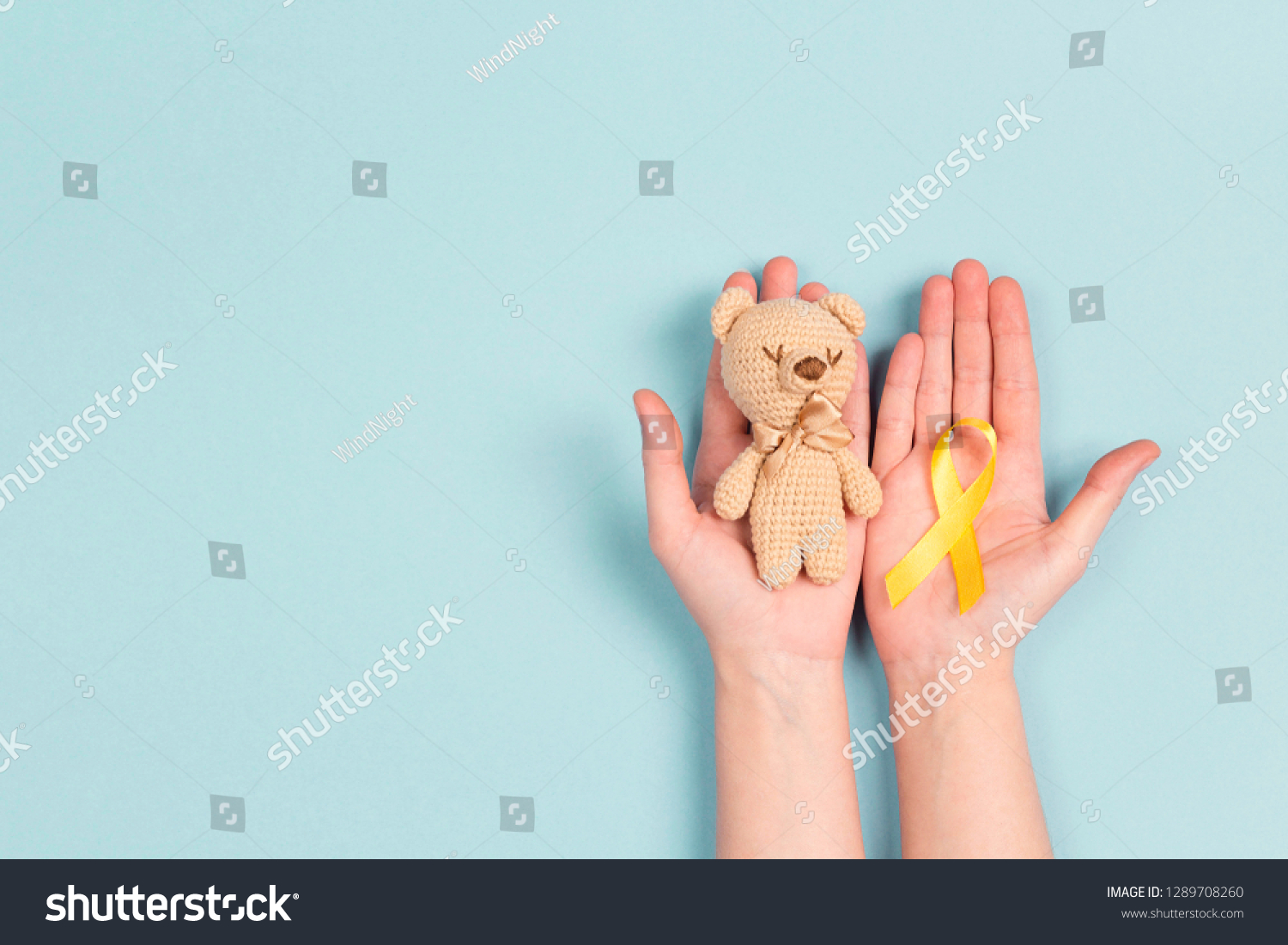 Girl hands holding children's toy with a Childhood Cancer Awareness Yellow Ribbon on blue background. Childhood Cancer Day February, 15. #1289708260