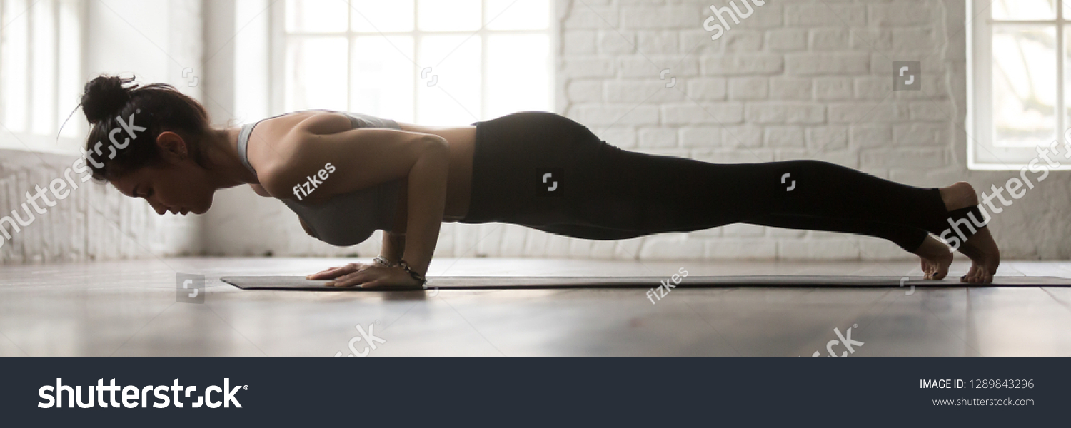 Horizontal full length side view photo young sporty woman wearing activewear doing yoga four limbed staff exercise chaturanga dandasana workout at home or sport center banner for website header design #1289843296