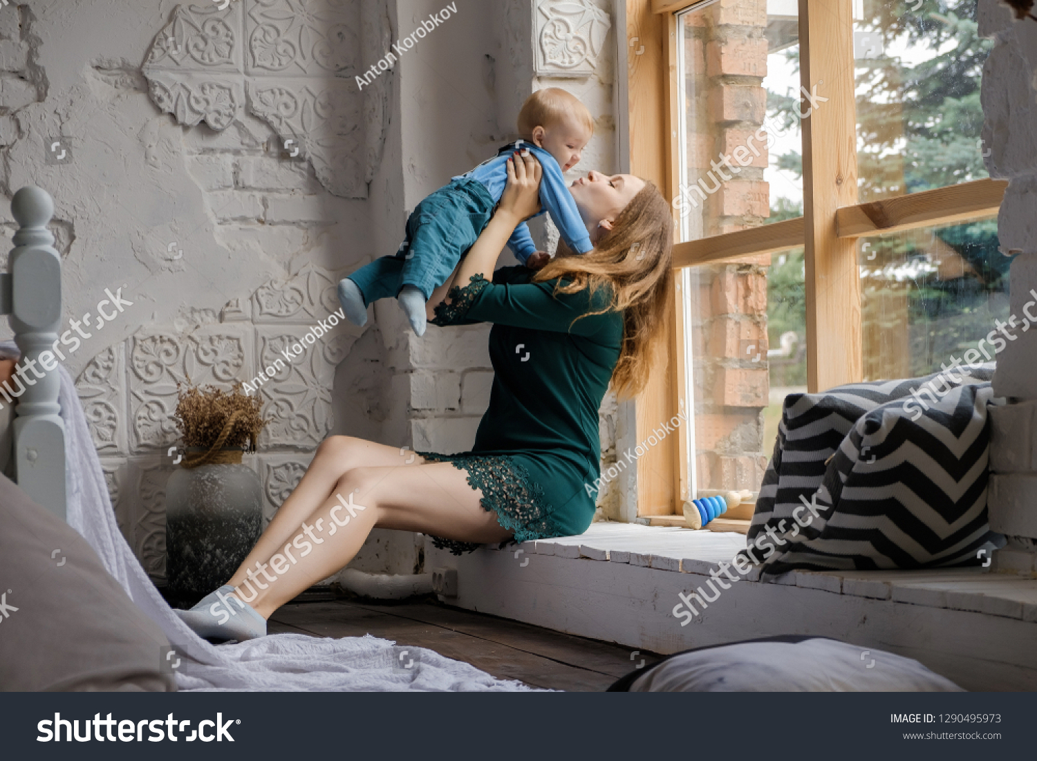 Young mom and beautiful baby sitting on the windowsill and playing. #1290495973