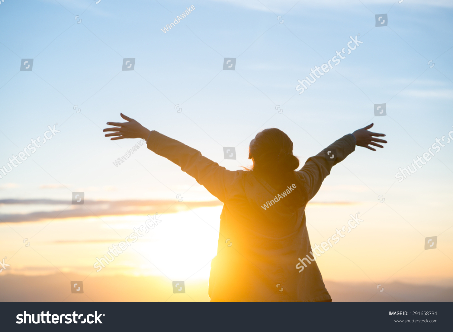 Happy woman standing alone with arms raised up during beautiful sunrise at the morning. #1291658734