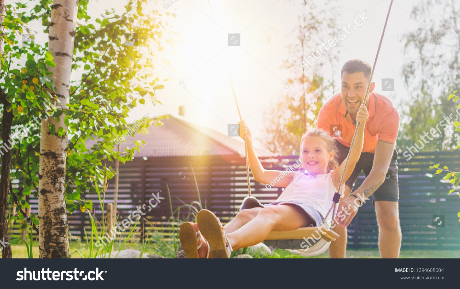 Joyous Father Pushes Swings with His Cute Little Daughter on Them. Happy Family Spends Time Together one Sunny Summer Day in the Idyllics Backyard. #1294608004
