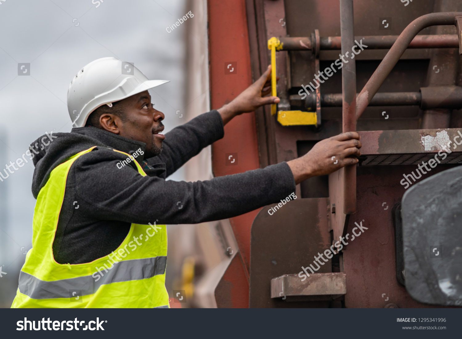 African American railroad engineer wearing safety equipment (helmet and jacket) checking gear train #1295341996