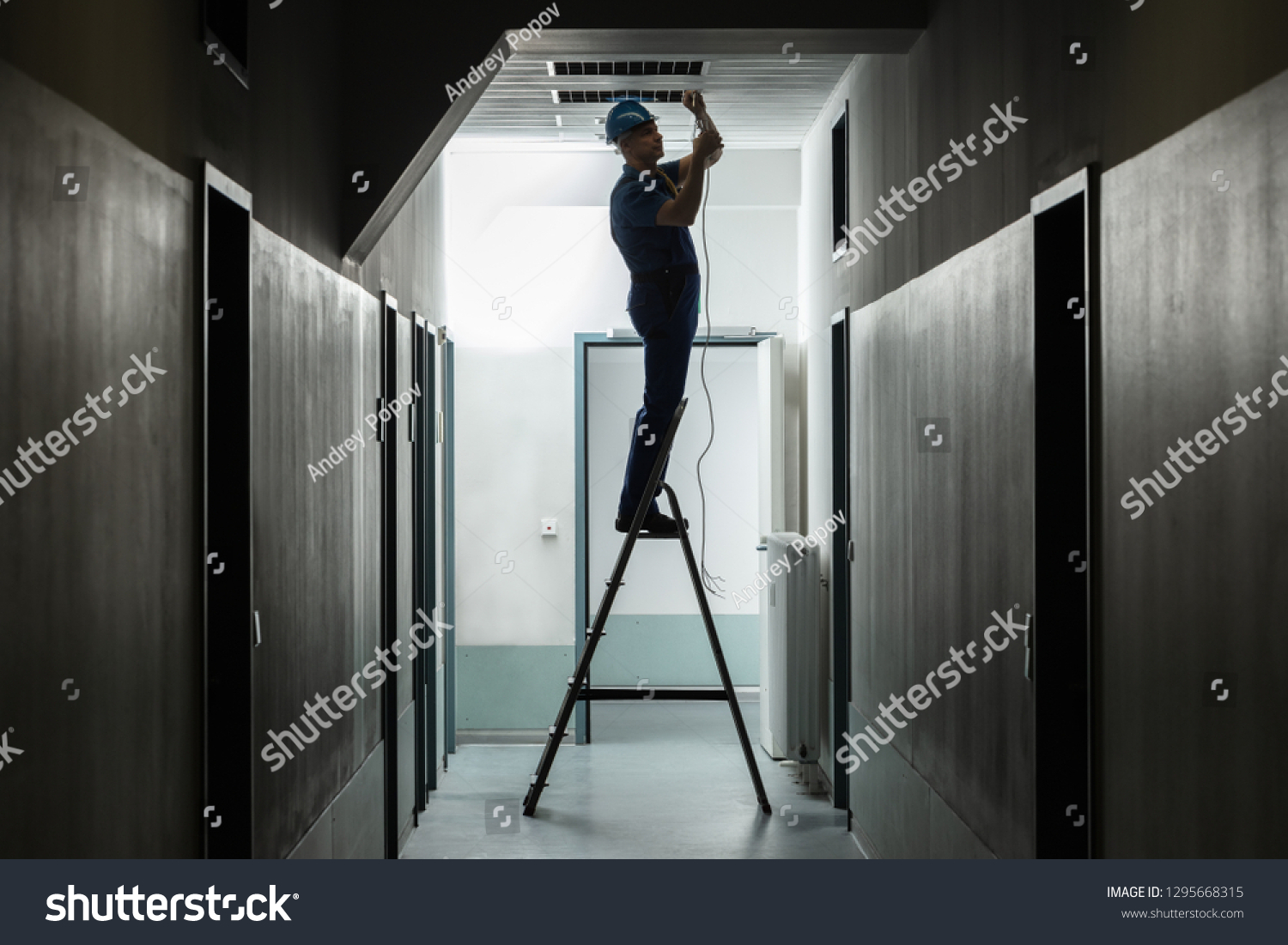 Silhouette Of A Male Electrician On Step Ladder Installing Light At Corridor #1295668315