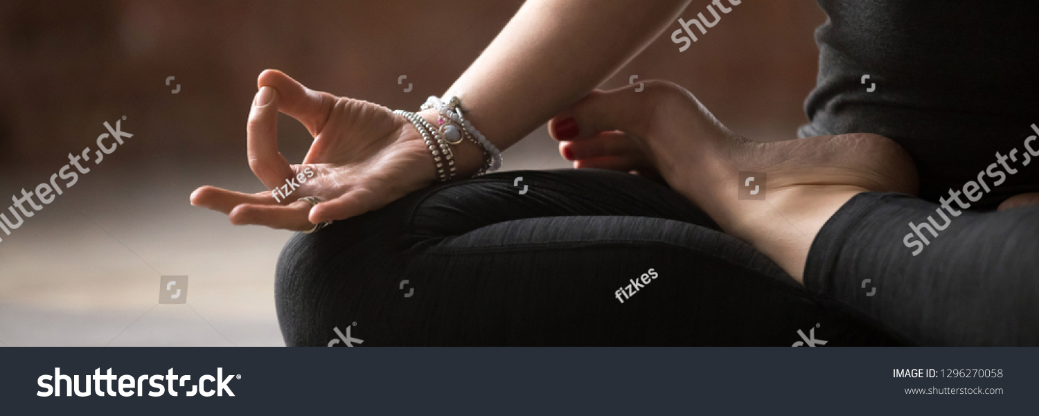 Close up female hand with bracelets fingers in Gyan mudra symbol of wisdom, girl wearing black activewear practice yoga sitting in lotus pose, banner for website header design with copy space for text #1296270058