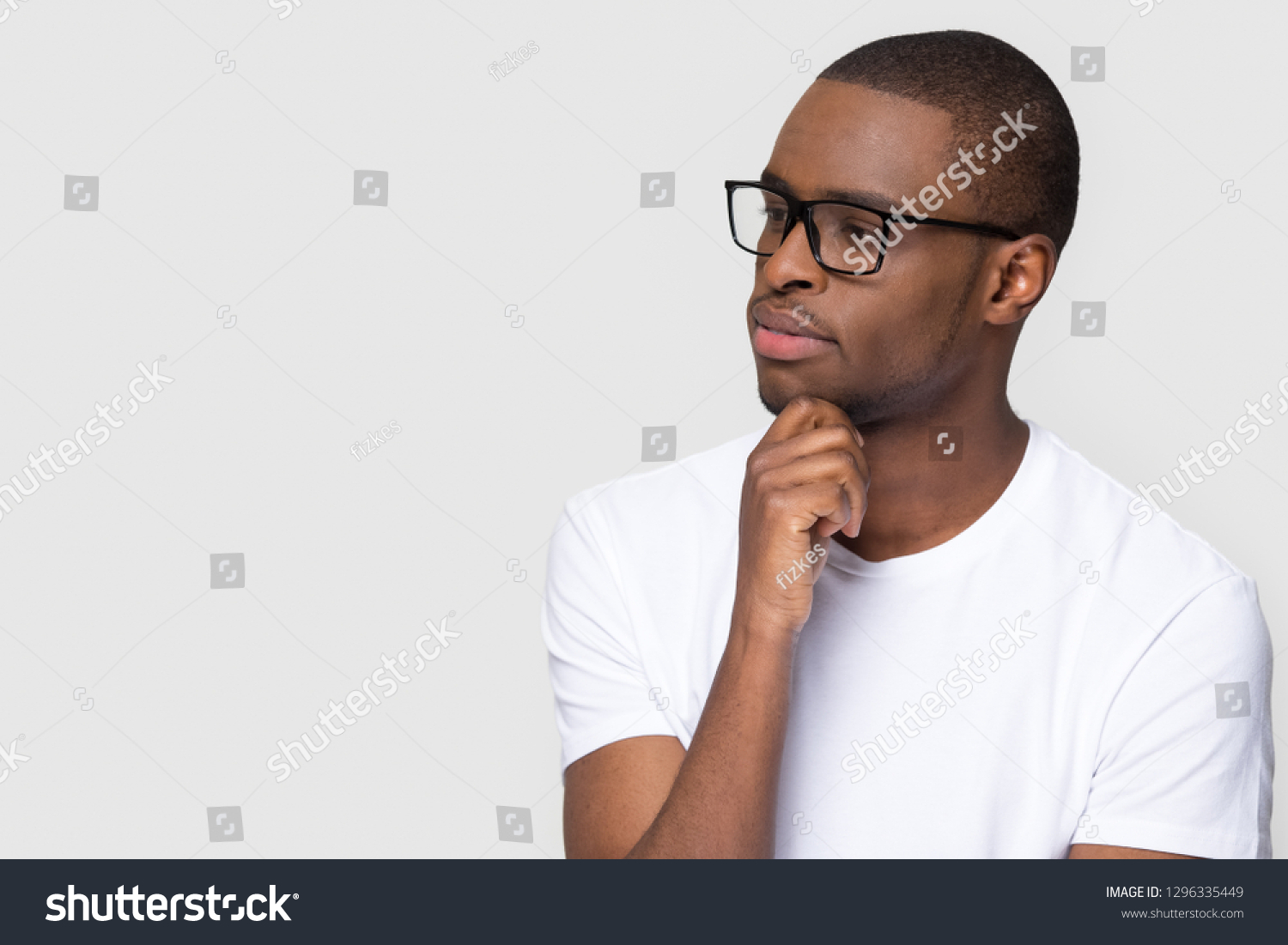 Thoughtful african man holding hand on chin looking at copy space feeling uncertain, doubtful black guy with unsure face thinking considering making decision isolated on white grey studio background #1296335449