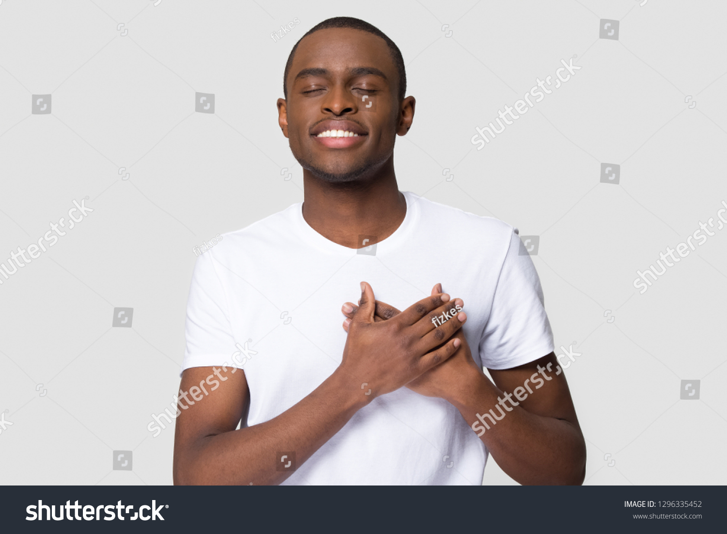 Grateful happy pleased african man holding hands on chest to heart feeling love appreciation gratitude honesty, thankful sincere proud black guy thanking isolated on white studio blank background #1296335452