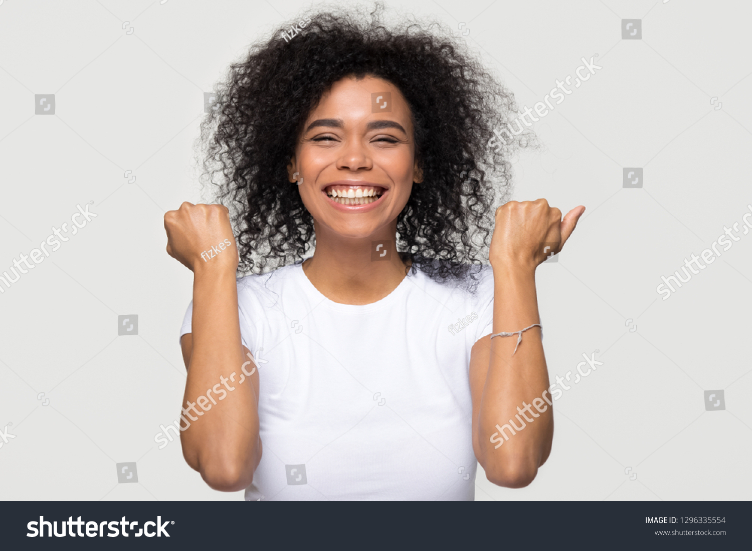 Excited happy young african american woman feeling overjoyed isolated at white grey studio background, lucky euphoric black girl winner celebrating win victory success raising hands in yes gesture #1296335554