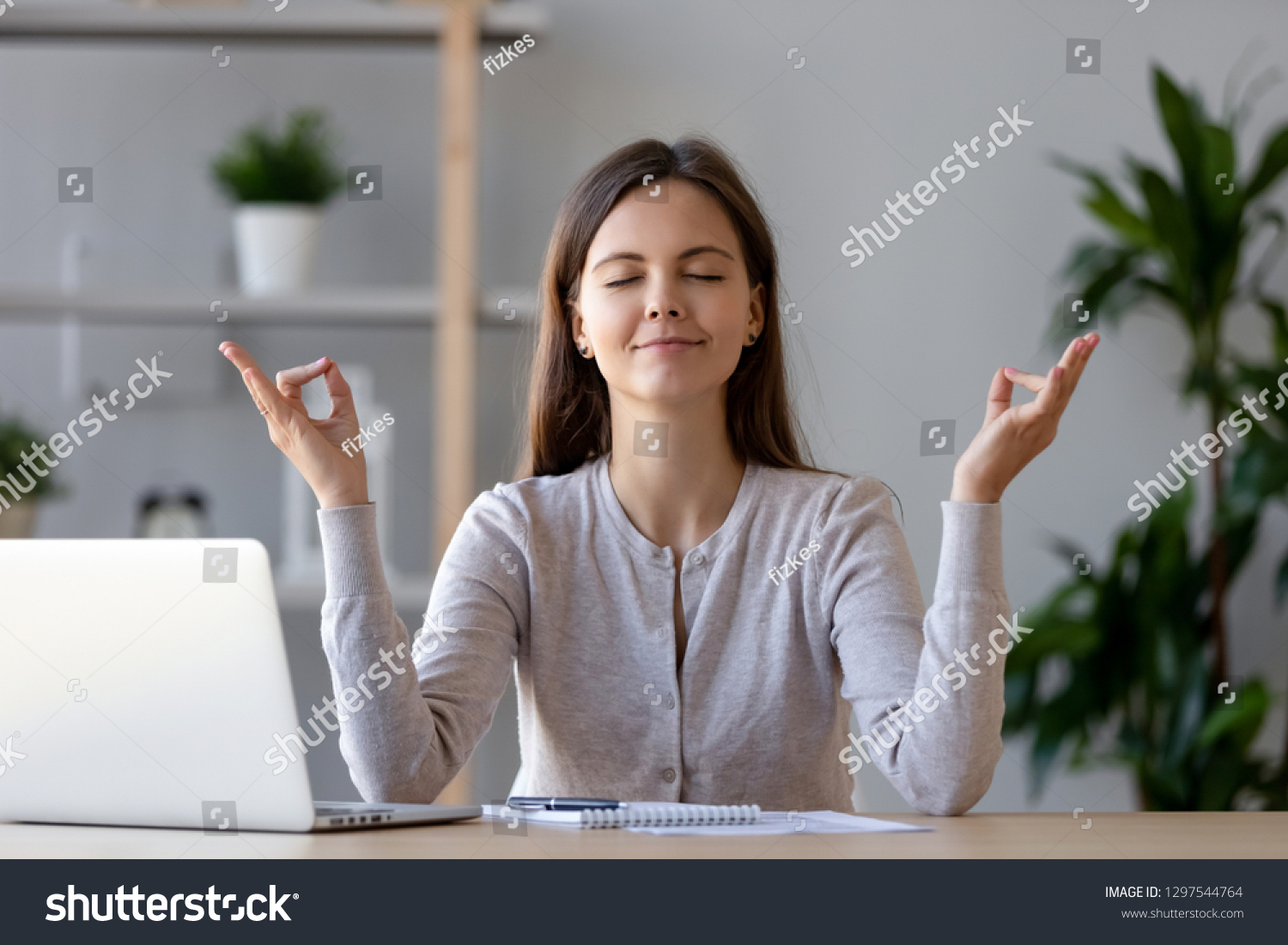 Calm young woman worker taking break doing yoga exercise at workplace, happy mindful female student meditating at home office desk feel balance harmony relaxation, stress relief zen at work concept #1297544764