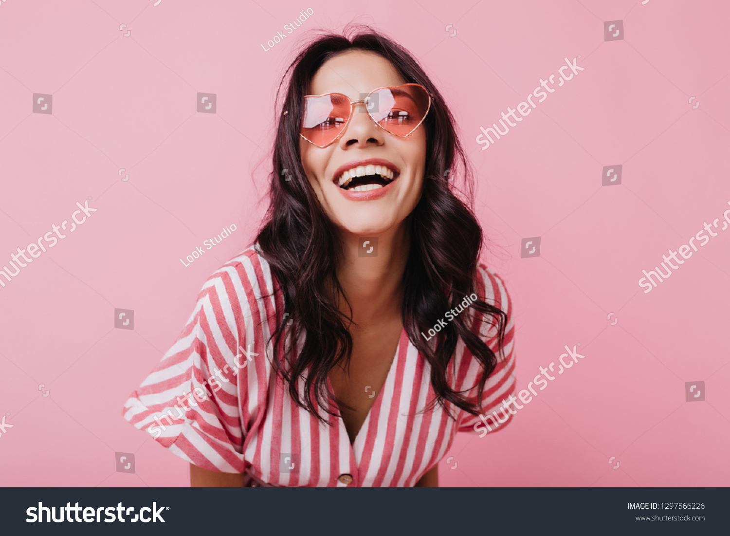 Emotional latin girl in sparkle sunglasses laughing to camera. Adorable female model enjoying photoshoot in pink clothes #1297566226