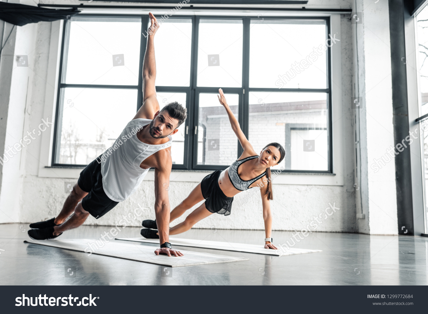 full length view of athletic young couple doing side plank exercise on yoga mats in gym #1299772684