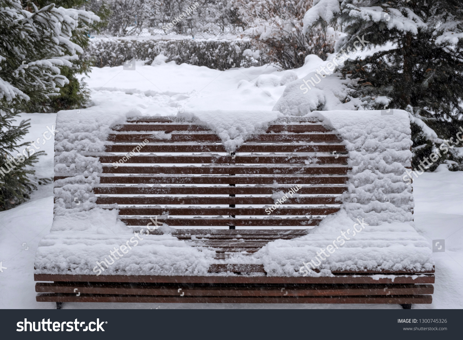Wooden bench covered with snow and heart drawn on it. Heart drawn on snow on bench in park. Saint Valentine's day. #1300745326