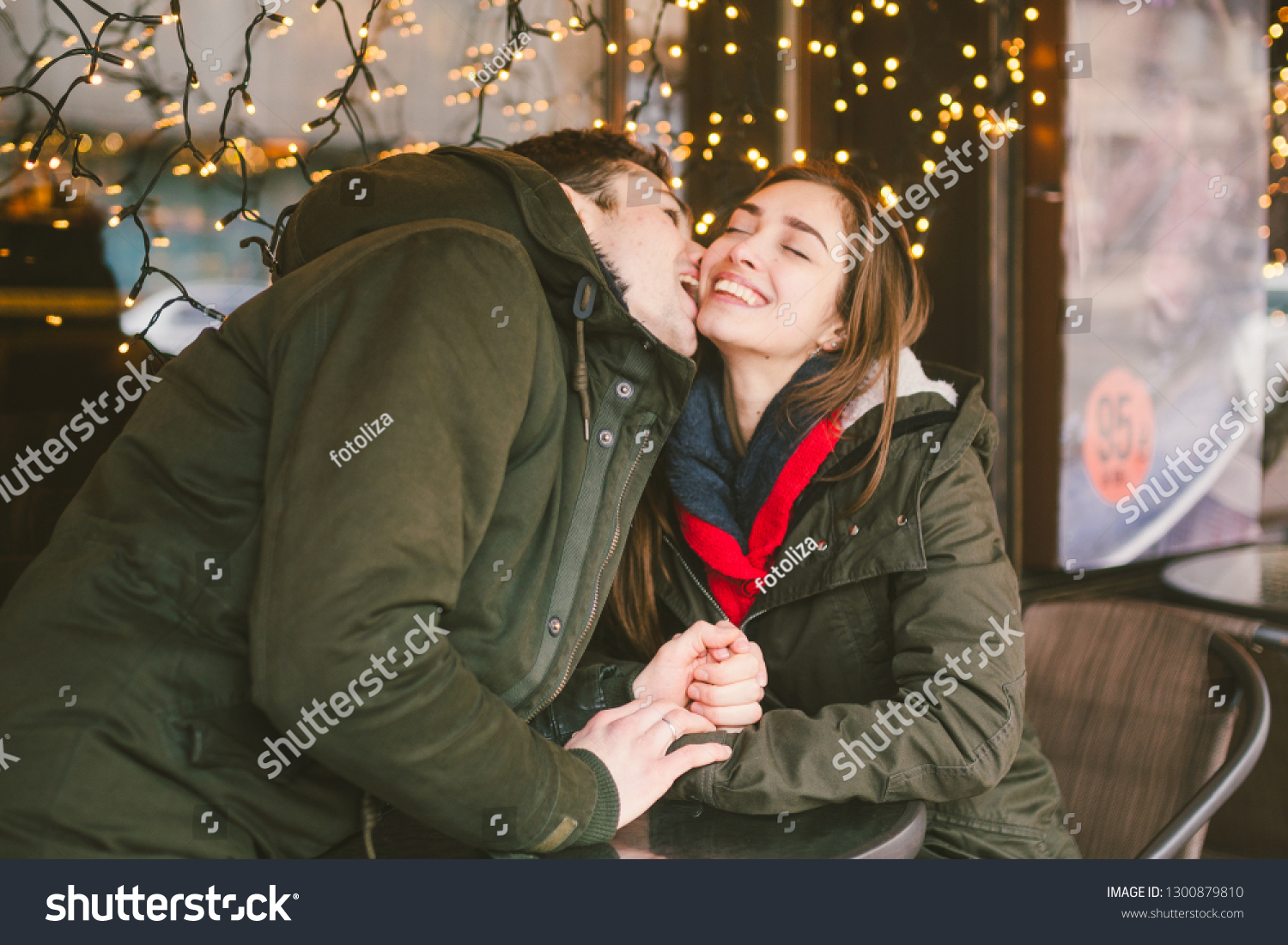 Theme love holiday Valentines Day. pair college students, Caucasian heterosexual lovers in winter, sit table of street cafe against the background window lights. Emotion romance of happiness and love. #1300879810