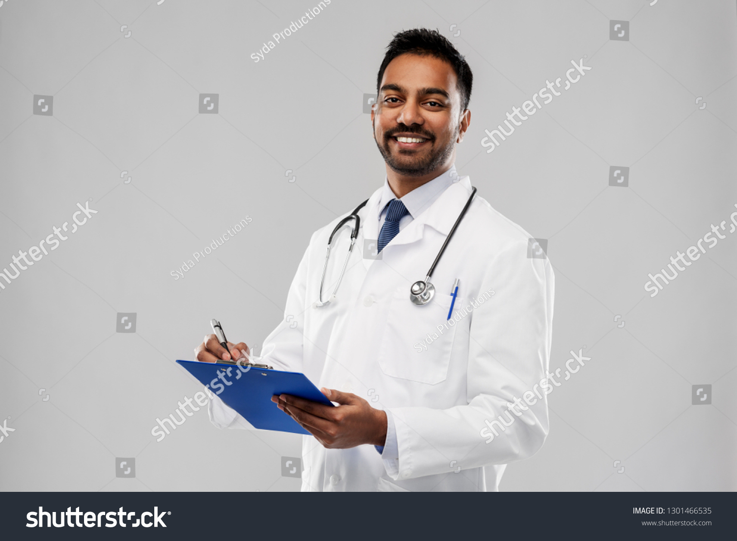 medicine, profession and healthcare concept - smiling indian male doctor in white coat with stethoscope and clipboard over grey background #1301466535