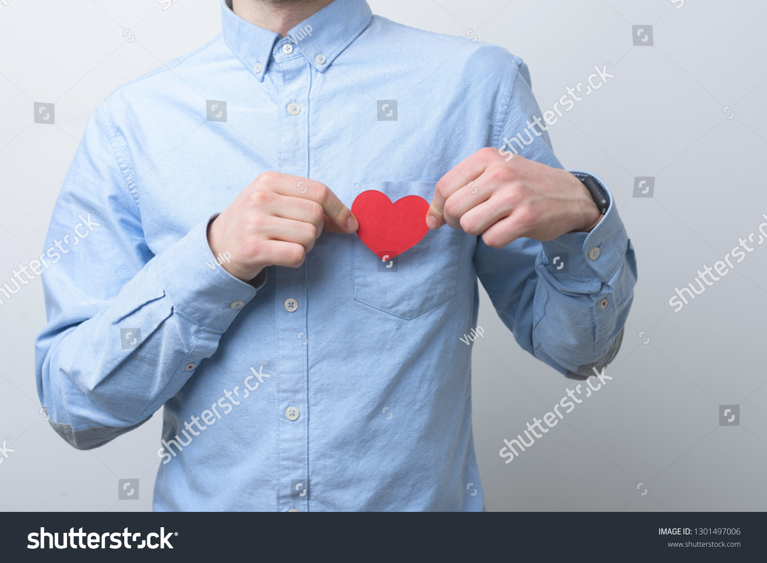 Man wearing a blue shirt is holding a small red heart above his chest. Caring and loving concept. #1301497006