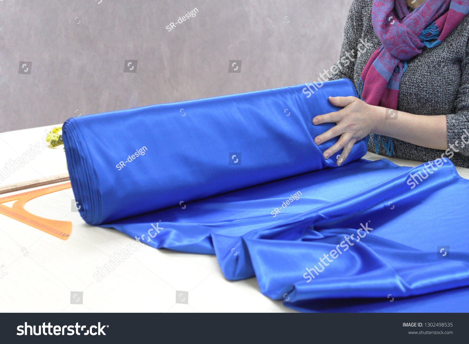 Woman tailor or seller of textiles unwinding a roll of fabric. Profession, atelier, textile shop #1302498535