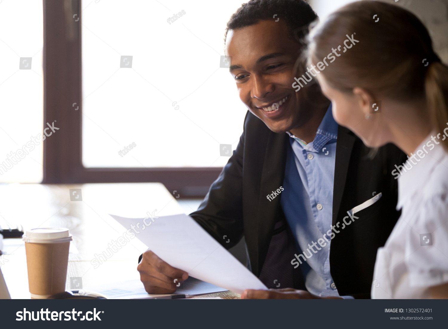 Smiling African American businessman holding female applicant cv, talking with candidate at work interview in office, excited black employer read employee resume at hiring. Recruitment concept #1302572401
