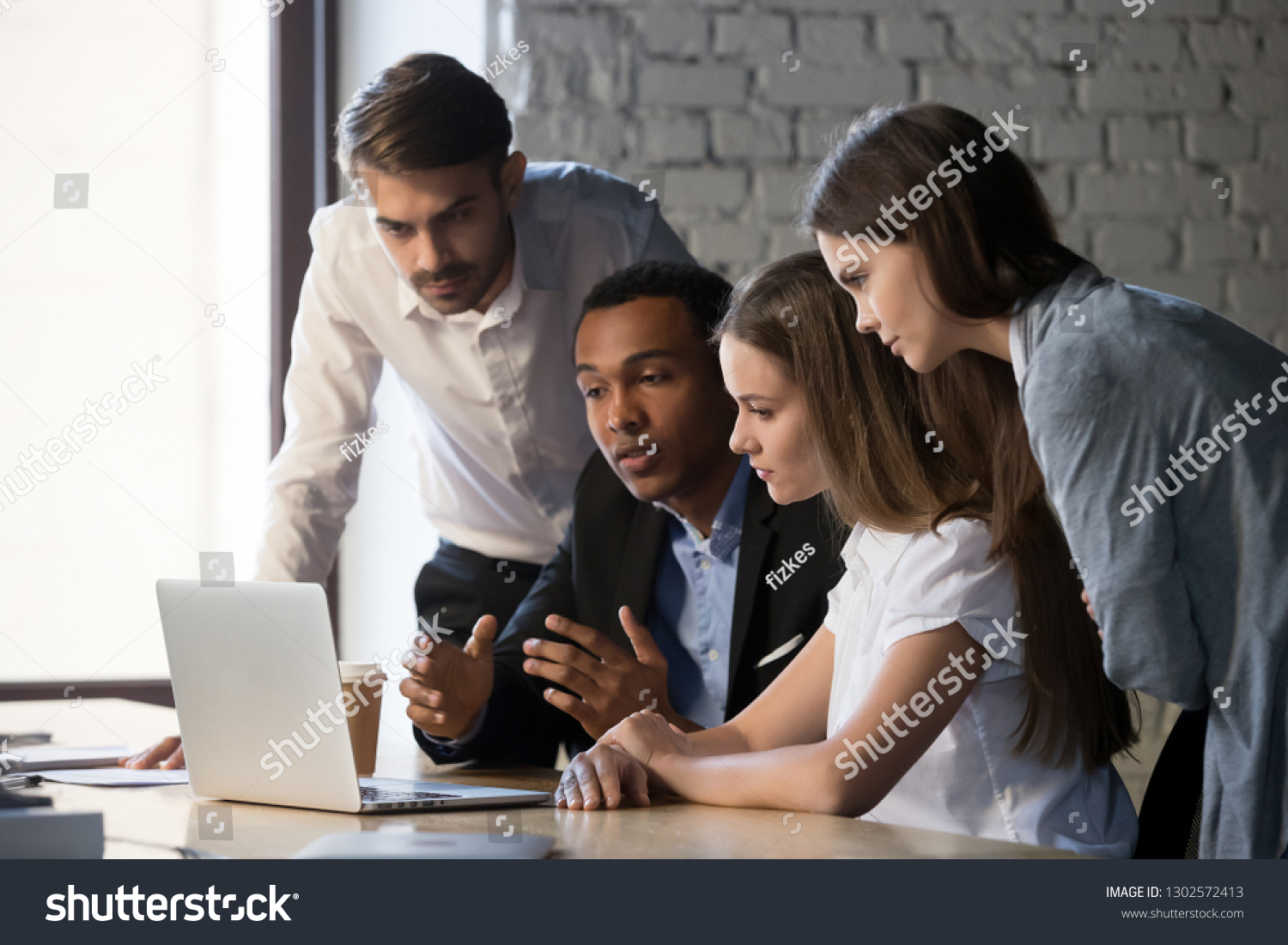 Diverse millennial workers cooperating, working together at laptop discussing business project in office, multiracial young businesspeople collaborate talking and sharing ideas on strategy success #1302572413