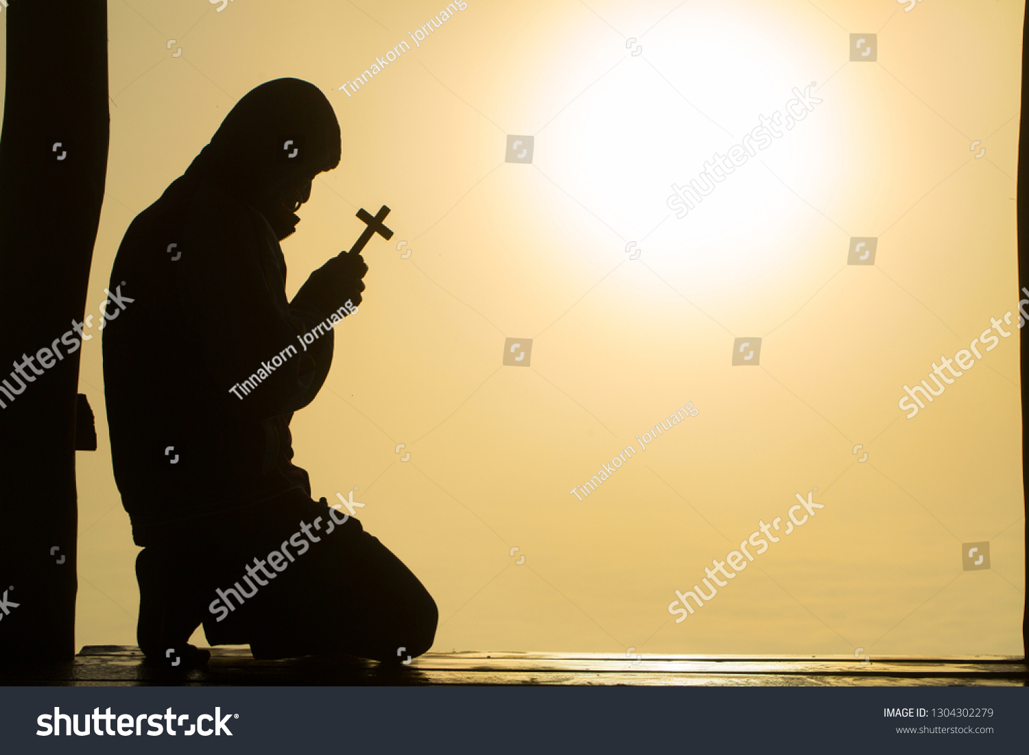 Silhouette of christian Man holding a cross cross in hands praying for blessing from god on sunlight background, hope concept #1304302279