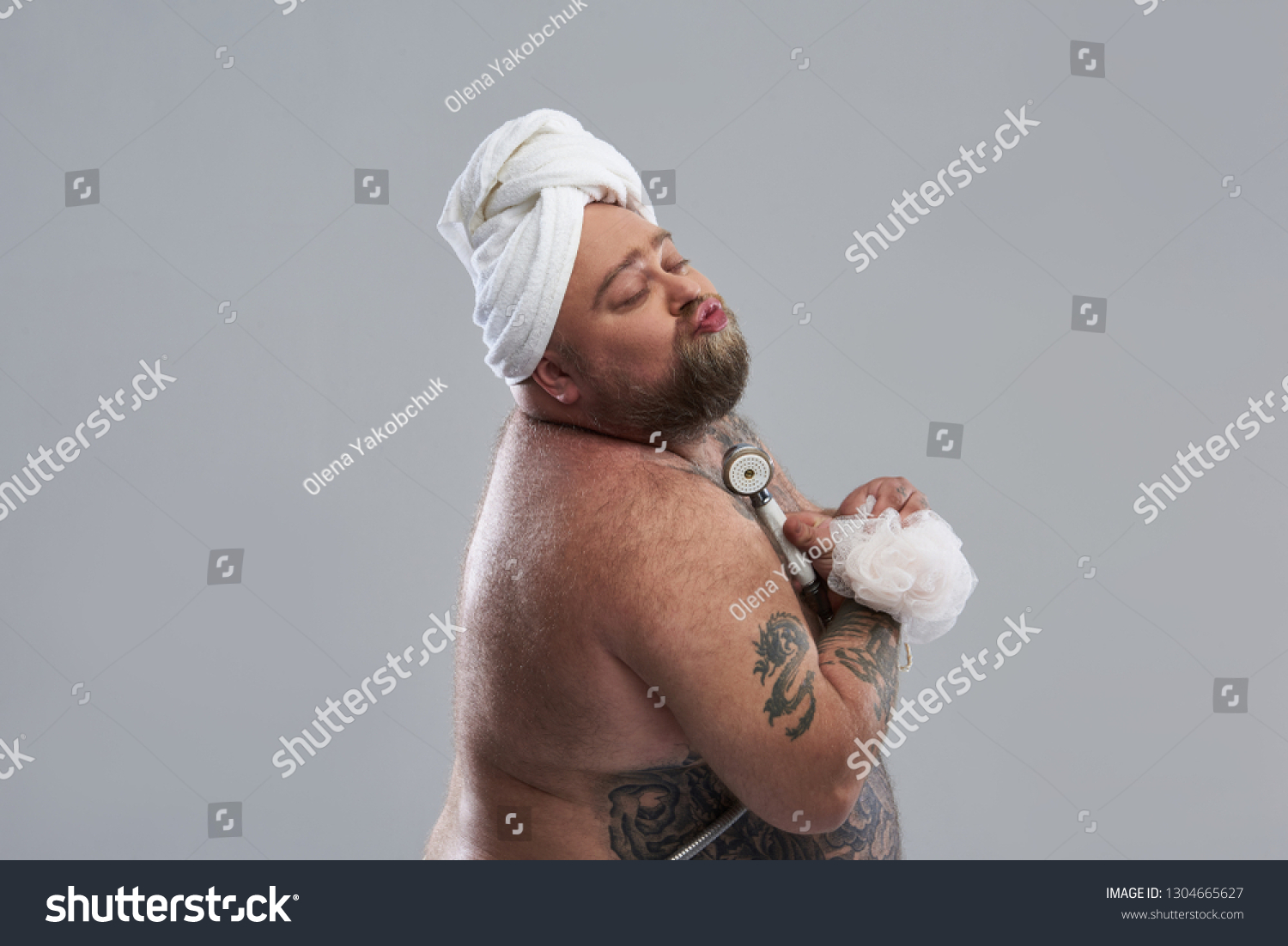 Hilarious tattooed fat man pretending to take shower with shower head and shower puff and looking funny. He giving kisses isolated on the grey background #1304665627