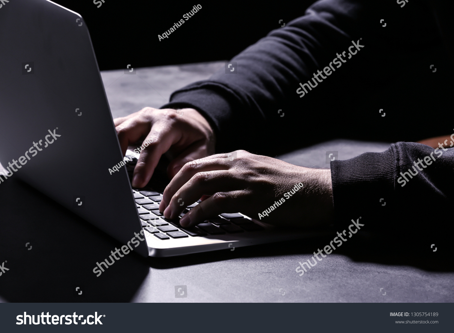 Professional hacker with laptop sitting at table on dark background, closeup #1305754189