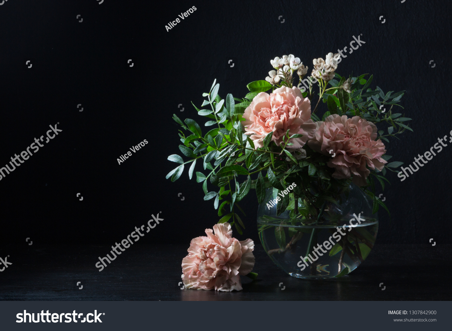 Carnations and pistachio sprigs in a glass vase with water, flower head next to the vase. #1307842900