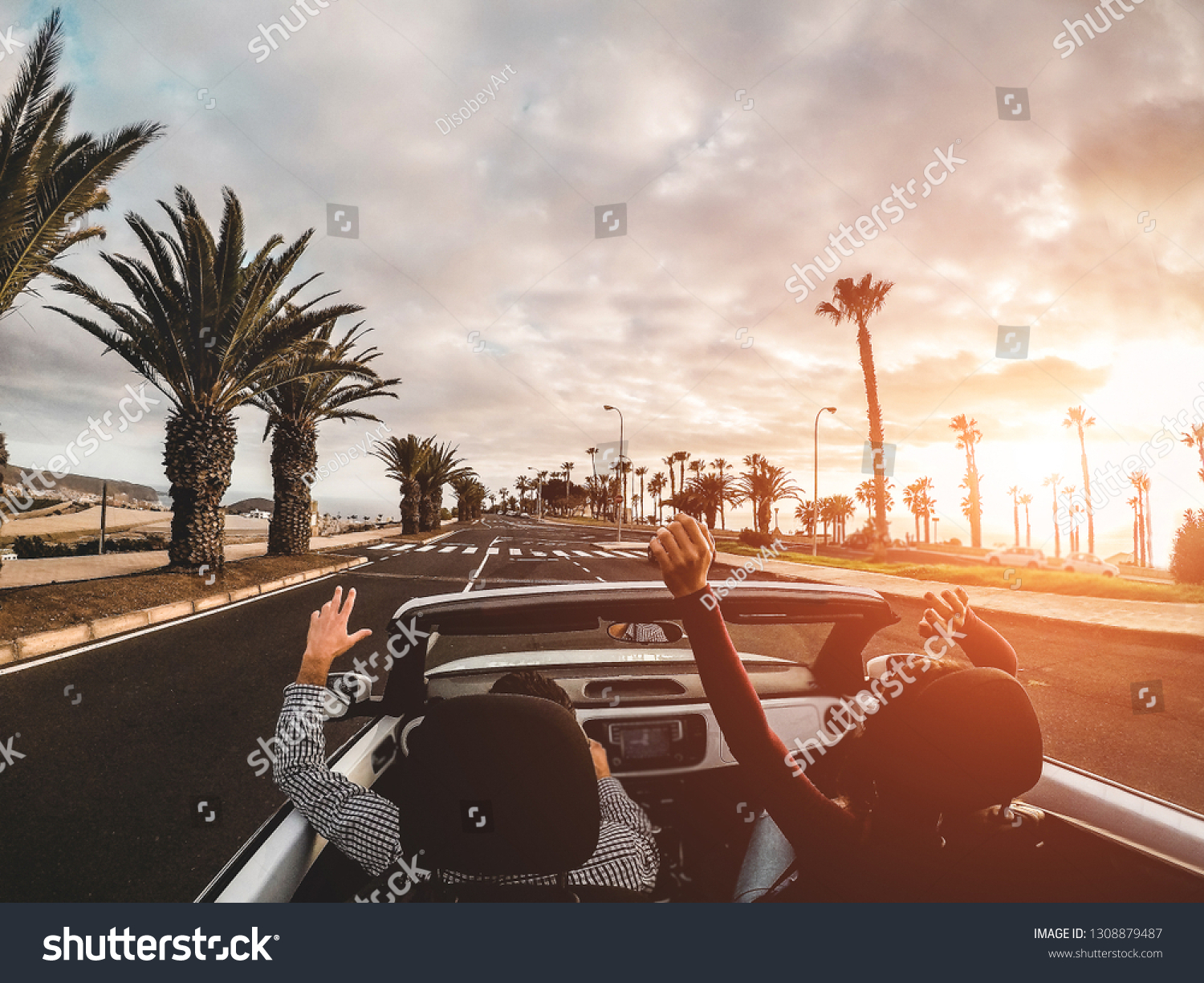 Happy people having fun in convertible car in summer vacation at sunset - Young couple enjoyng  holiday on cabrio auto outdoor - Travel, youth lifestyle and wanderlust concept - Focus on hands #1308879487