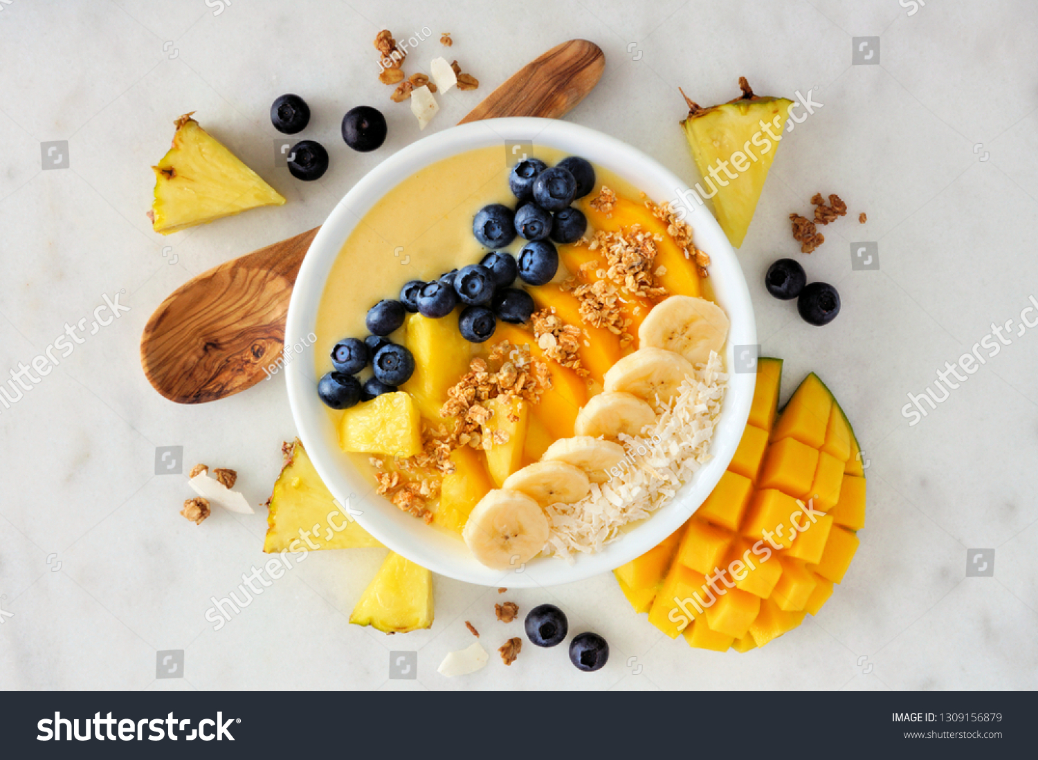 Healthy pineapple, mango smoothie bowl with coconut, bananas, blueberries and granola. Above view scene on a bright background. #1309156879