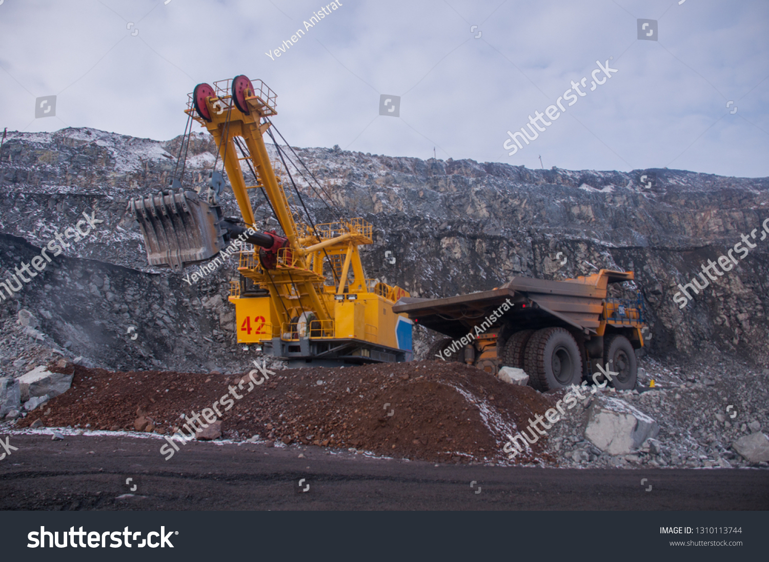 Excavator in the quarry loads the dumper with iron ore. Loading in winter #1310113744