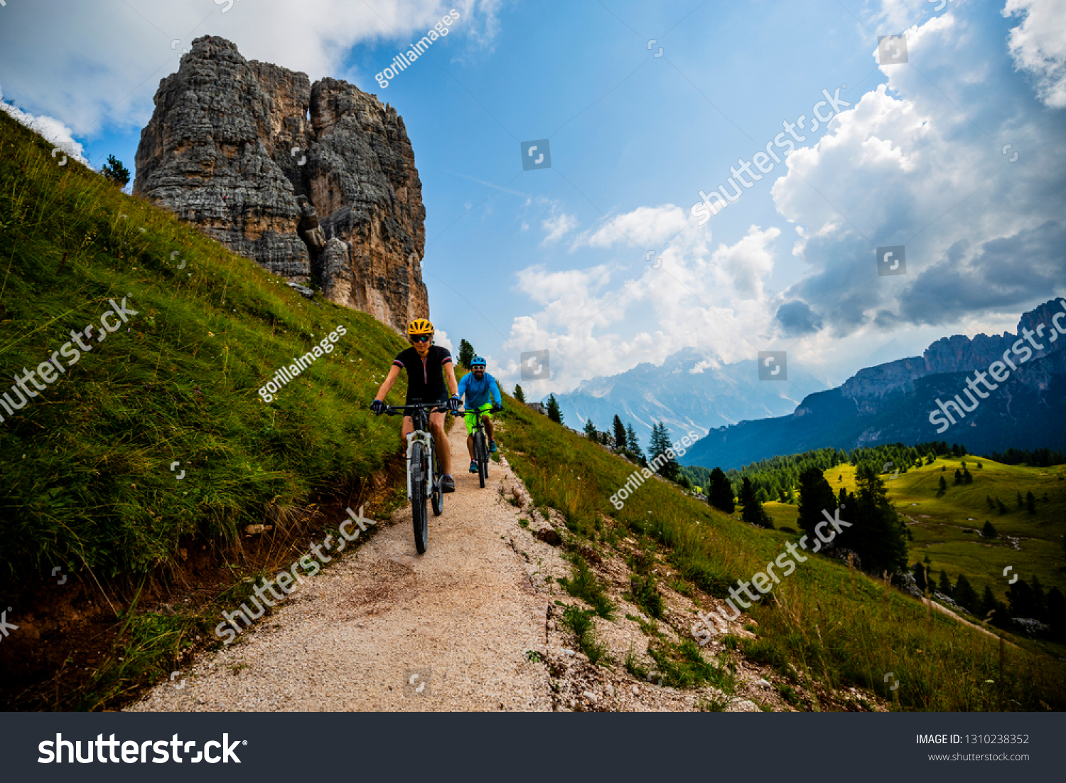 Couple cycling in Cortina d'Ampezzo, stunning Cinque Torri and Tofana in background. Woman and man riding MTB trail. South Tyrol province of Italy, Dolomites. #1310238352