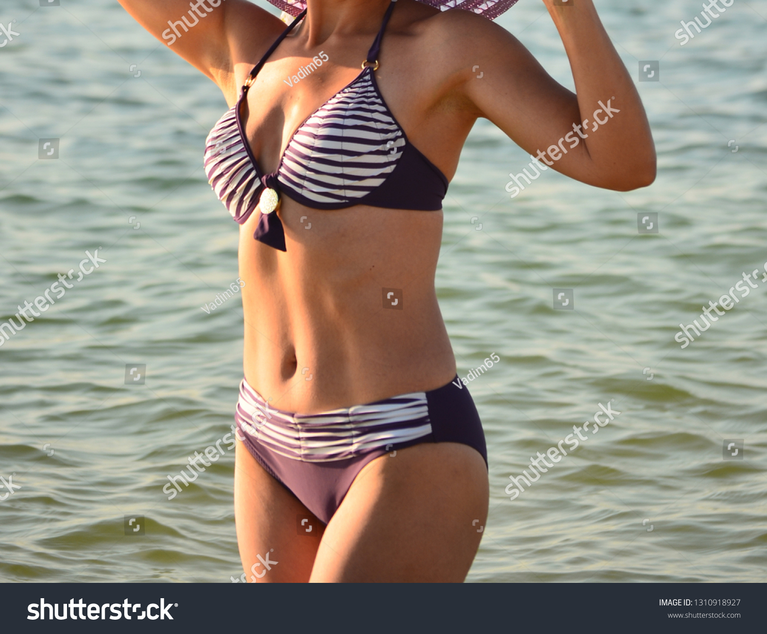 A woman in a gray swimsuit is standing near the sea and posing for a photo shoot #1310918927