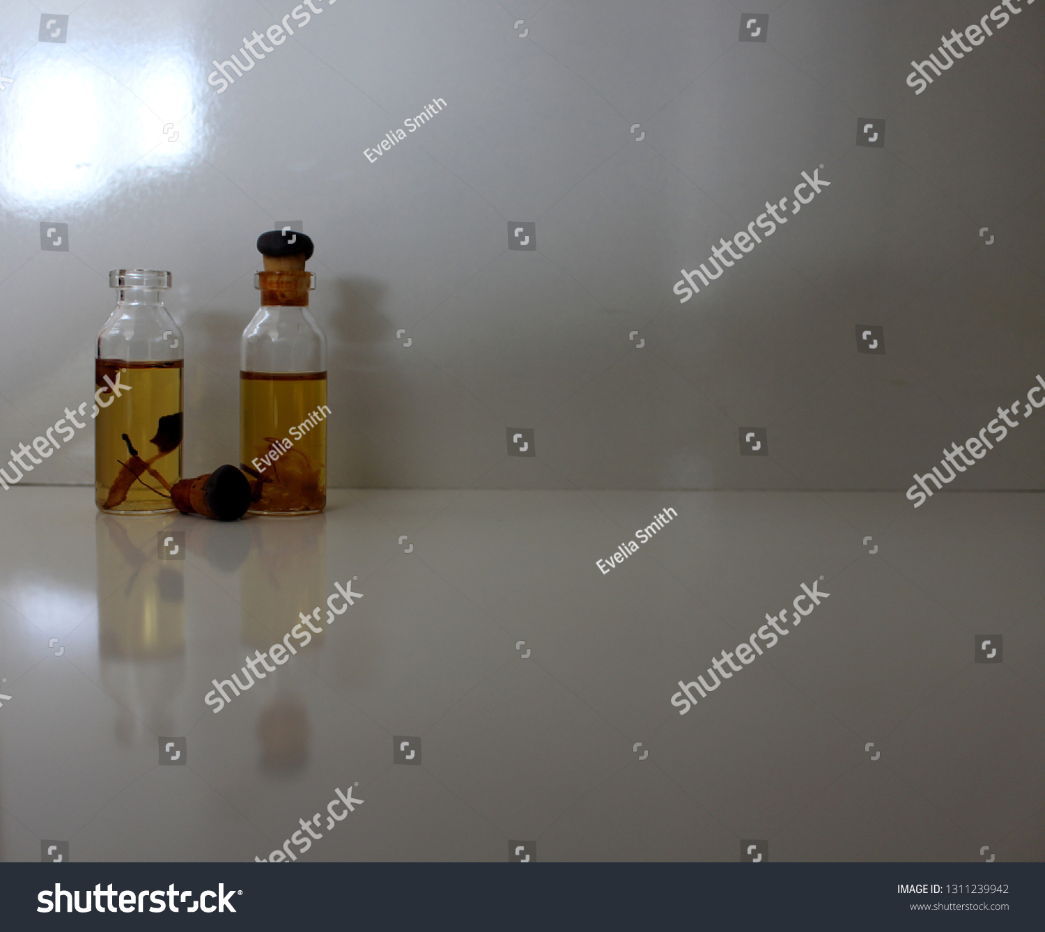 Two bottles of natural perfume, one open, containing plants, on white background #1311239942