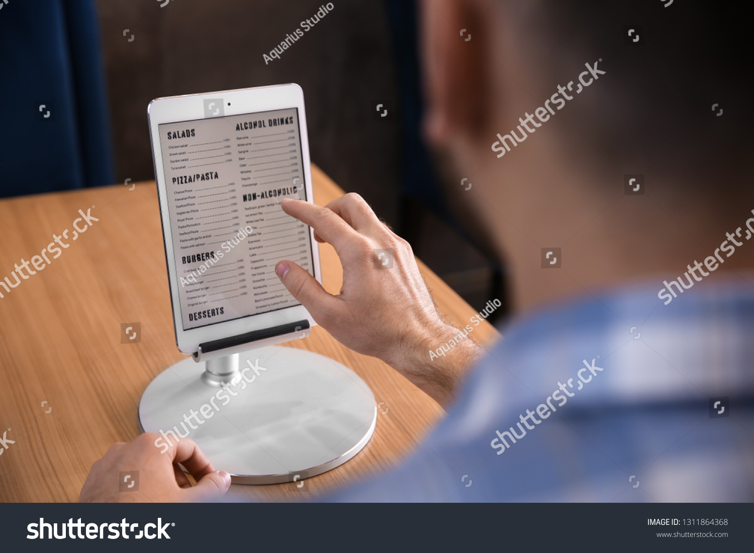 Young man with tablet PC looking through menu in restaurant #1311864368