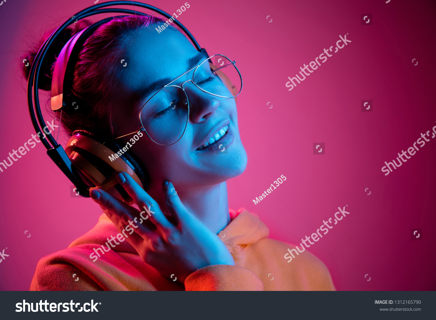 Fashion pretty woman with headphones listening to music over red neon background at studio. #1312165790