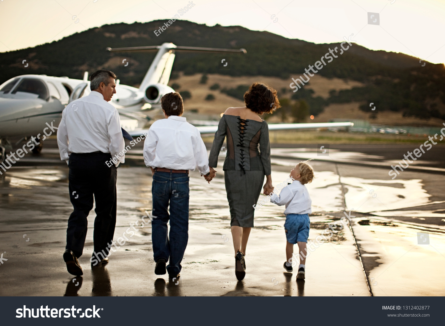 Family walking towards a private jet holding hands #1312402877