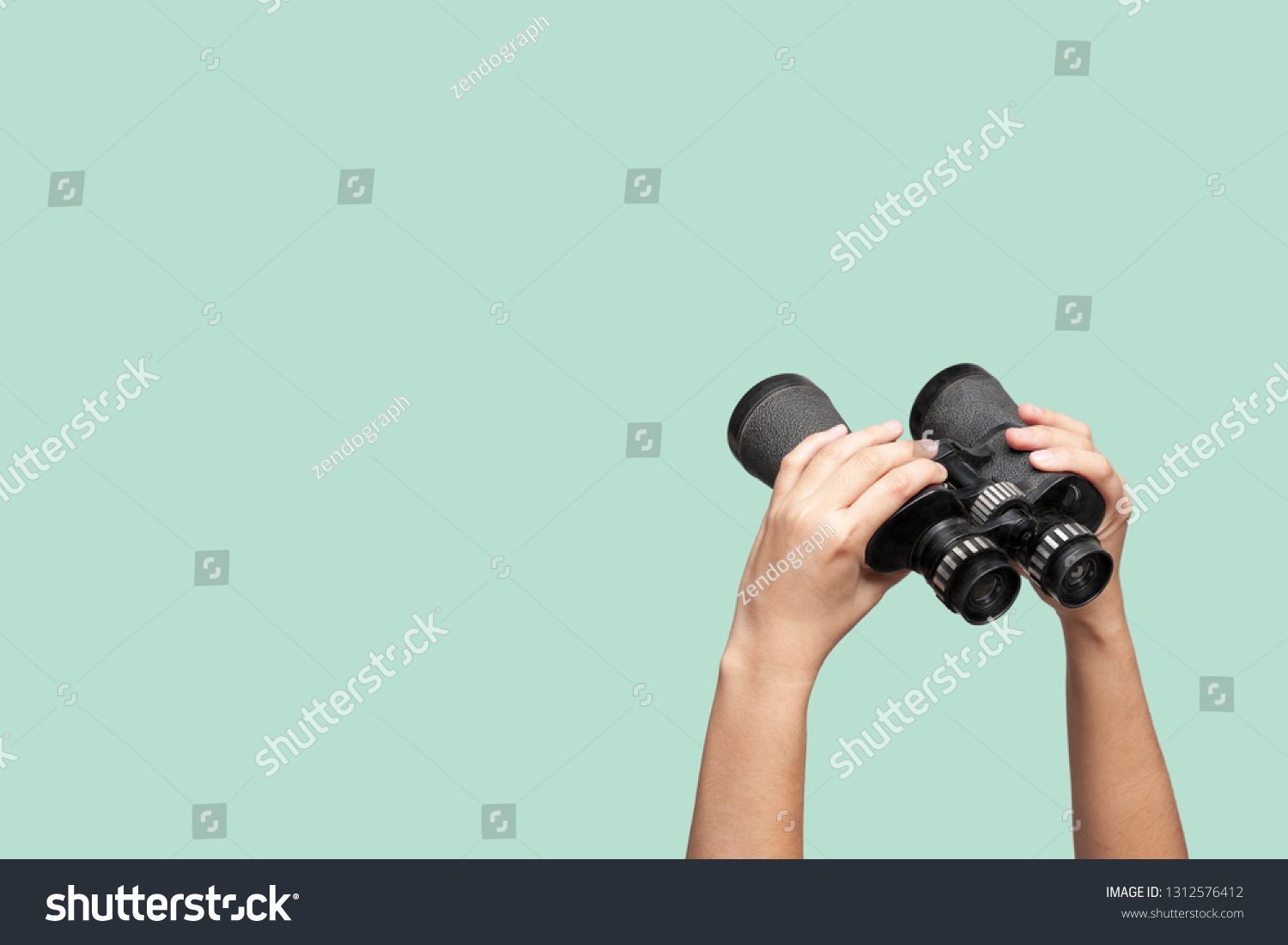 Hands holding binoculars on green background, looking through binoculars, journey, find and search concept. #1312576412