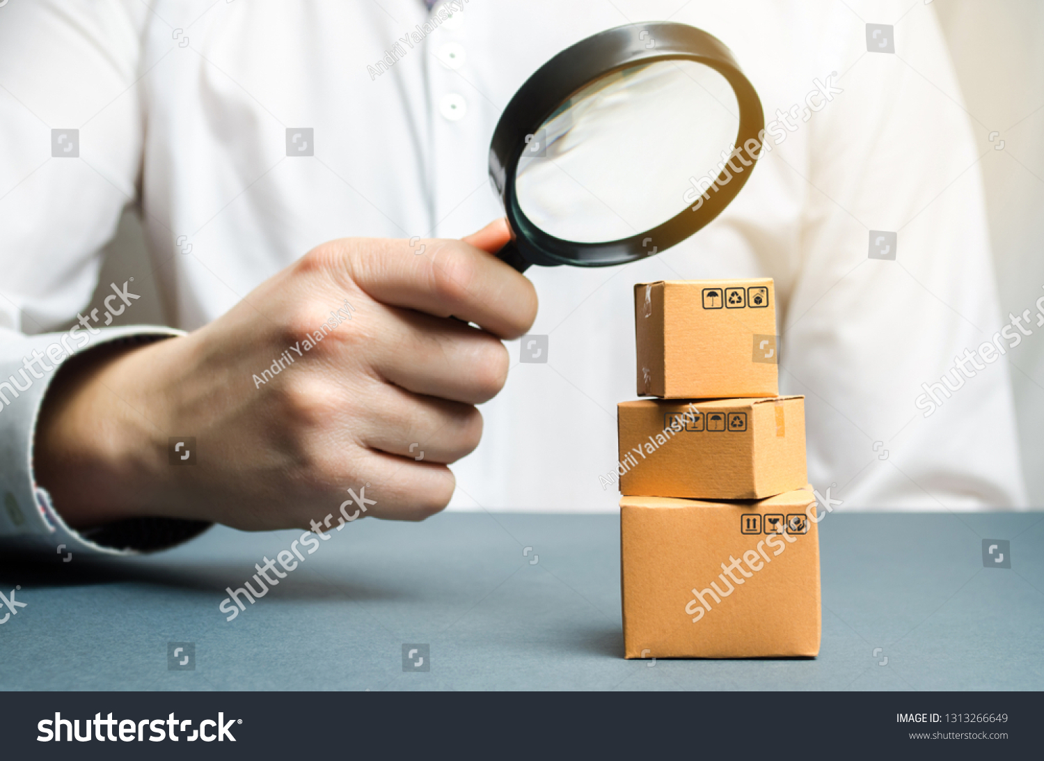 A man holds a magnifying glass above the boxes. Examination of goods for the presence of contraband, prohibited goods, defects. Quality control, authentication. study of consumer sentiment #1313266649