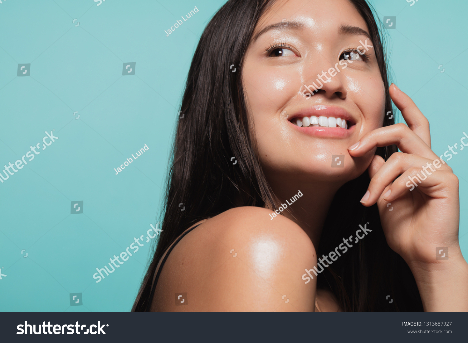 Close up of cute asian girl with glowing skin against blue background. Beautiful face of girl with fresh healthy skin. #1313687927