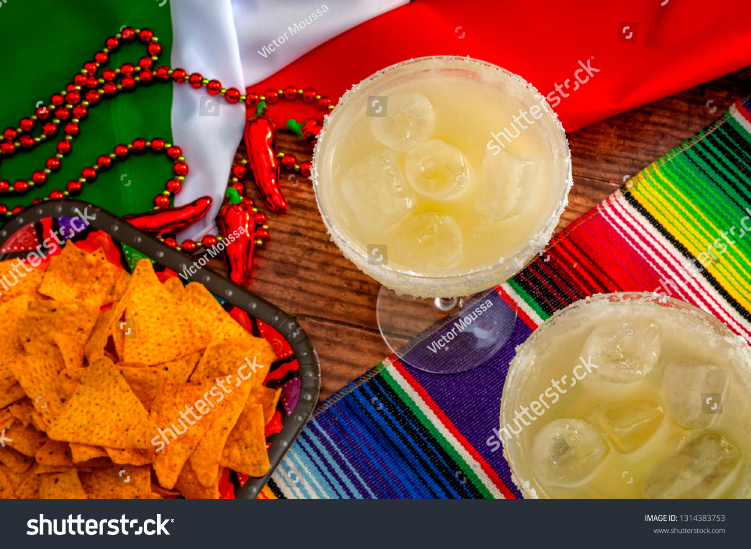 Mexican fiesta and Cinco de Mayo party concept theme with jalapeno pepper beads necklace, traditional rug or serape, two margarita glasses, chips and the flag of Mexico #1314383753
