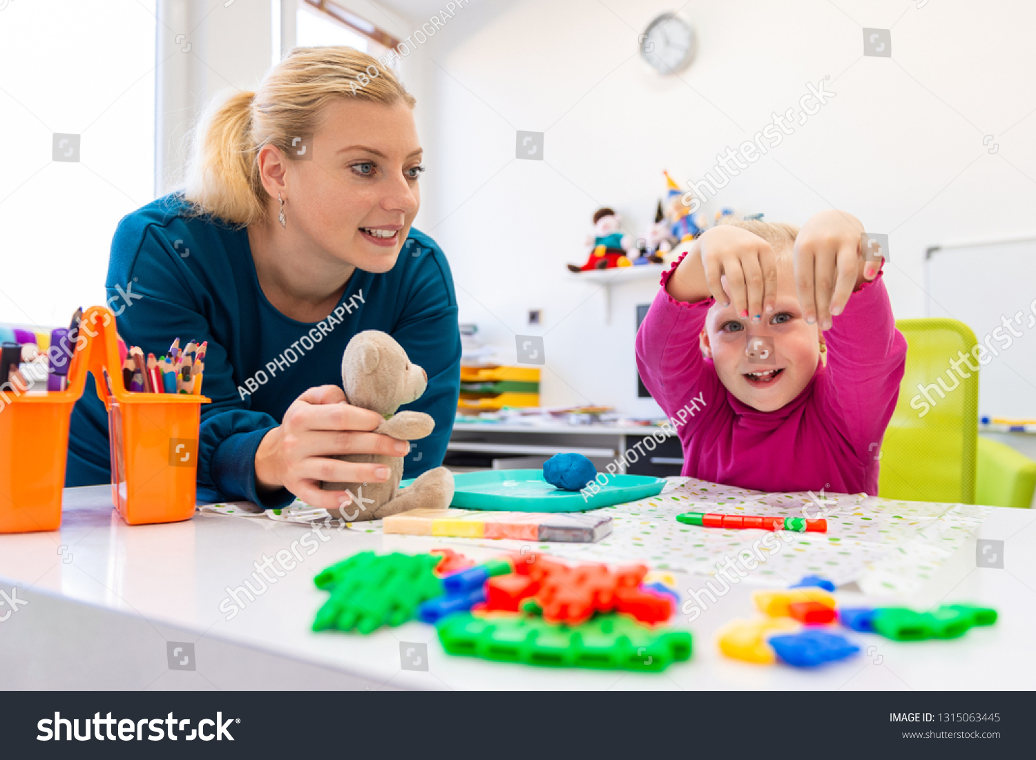 Toddler girl in child occupational therapy session doing sensory playful exercises with her therapist.  #1315063445