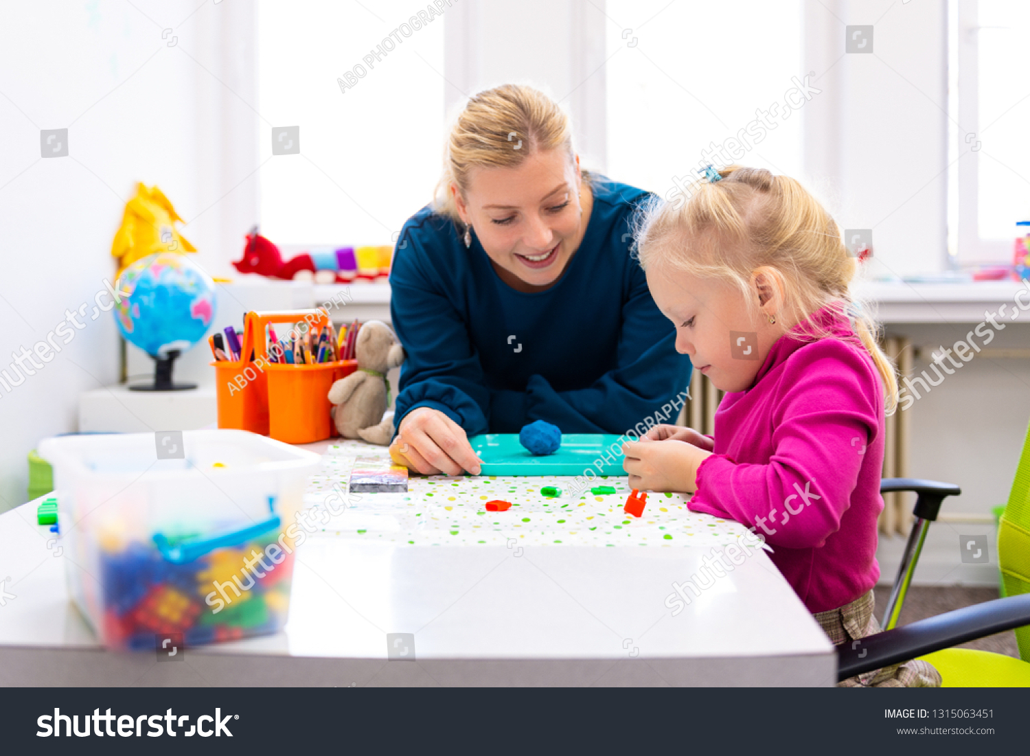 Toddler girl in child occupational therapy session doing sensory playful exercises with her therapist.  #1315063451
