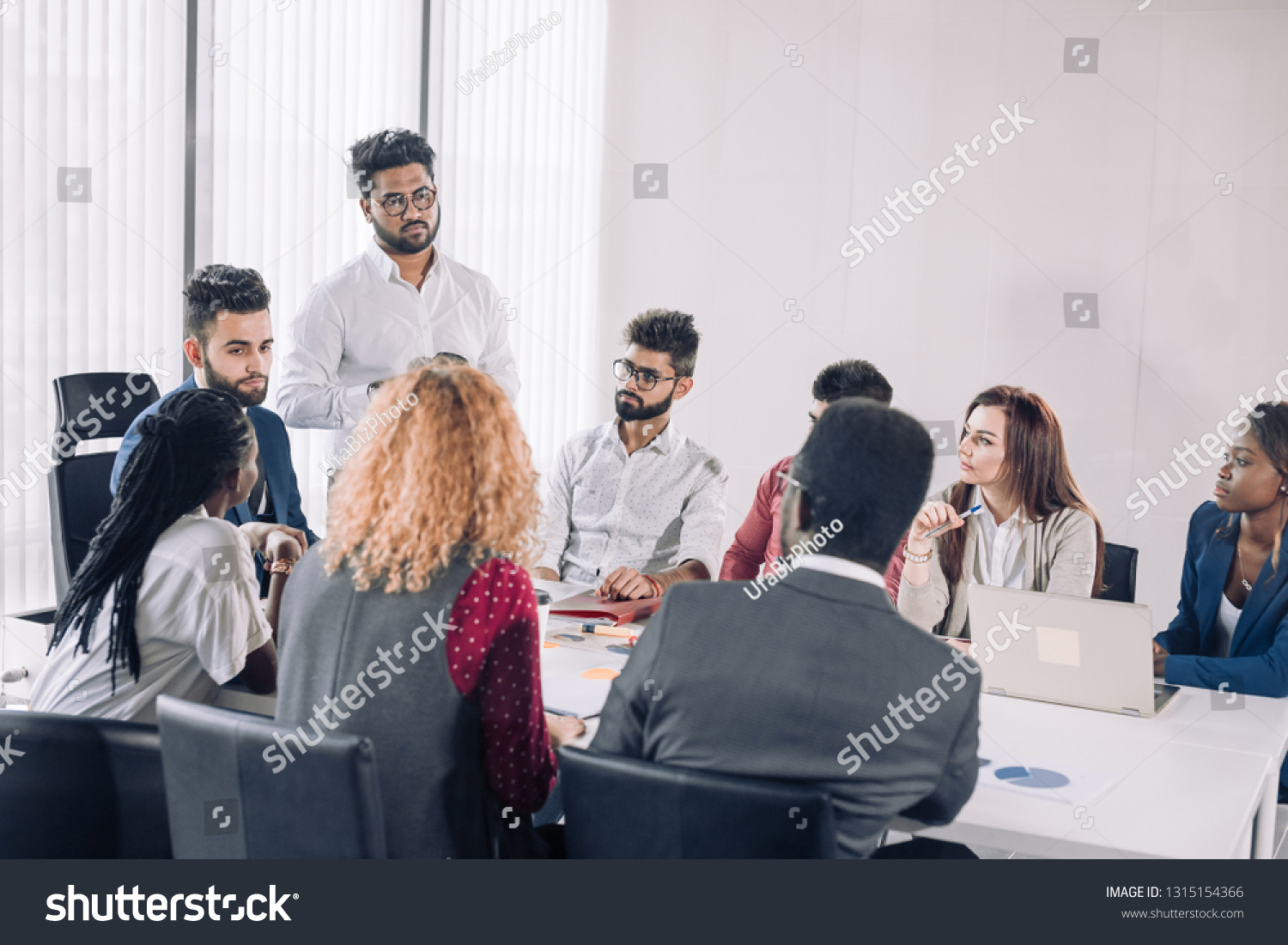Young interracial coworkers sitting at open space office together, working on laptops, collaborating in modern office interior with panoramic windows. Teamwork Concept #1315154366