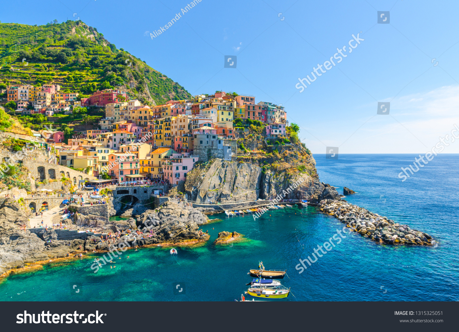 Manarola traditional typical Italian village in National park Cinque Terre, colorful multicolored buildings houses on rock cliff, fishing boats on water, blue sky background, La Spezia, Liguria, Italy #1315325051