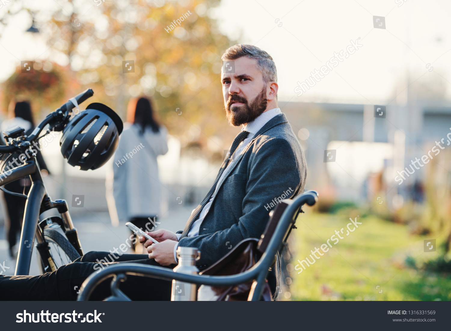 Businessman commuter with bicycle and smartphone sitting on bench in city. #1316331569