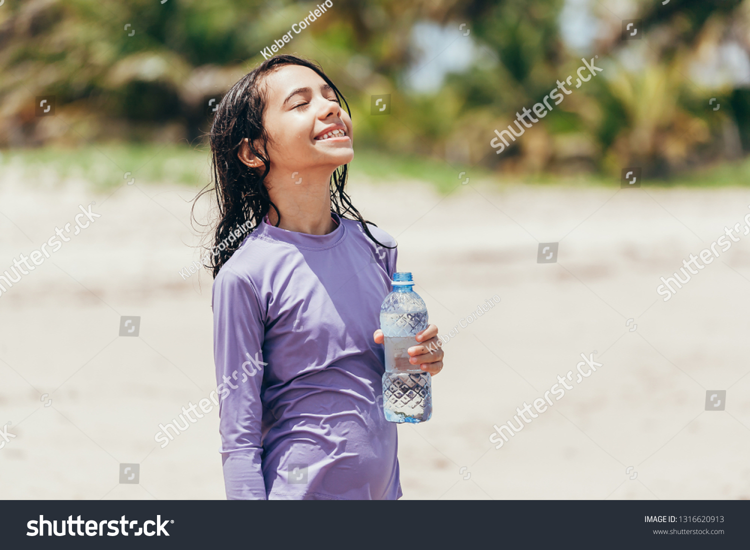 Portrait of little girl drinking water on the beach #1316620913