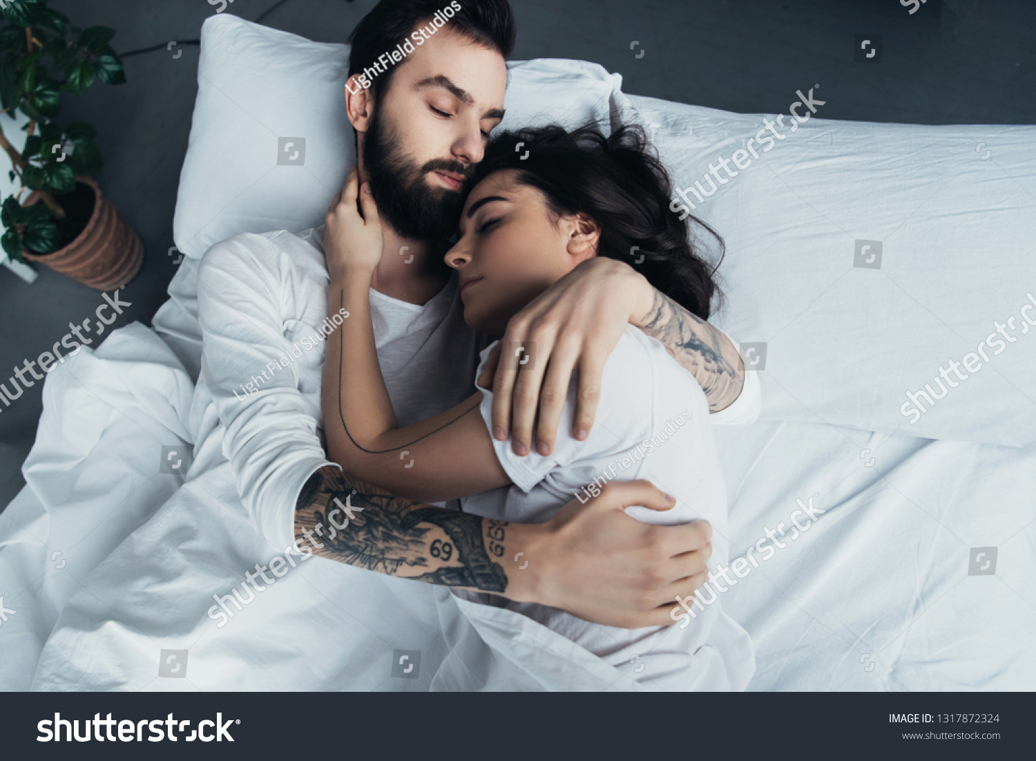 beautiful young tattooed couple embracing while sleeping in bed #1317872324