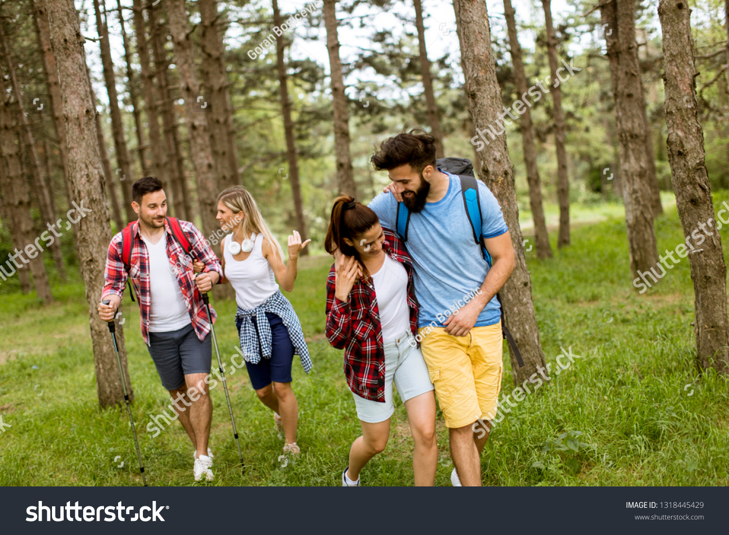 Group of four friends hiking together through a forest at sunny day #1318445429