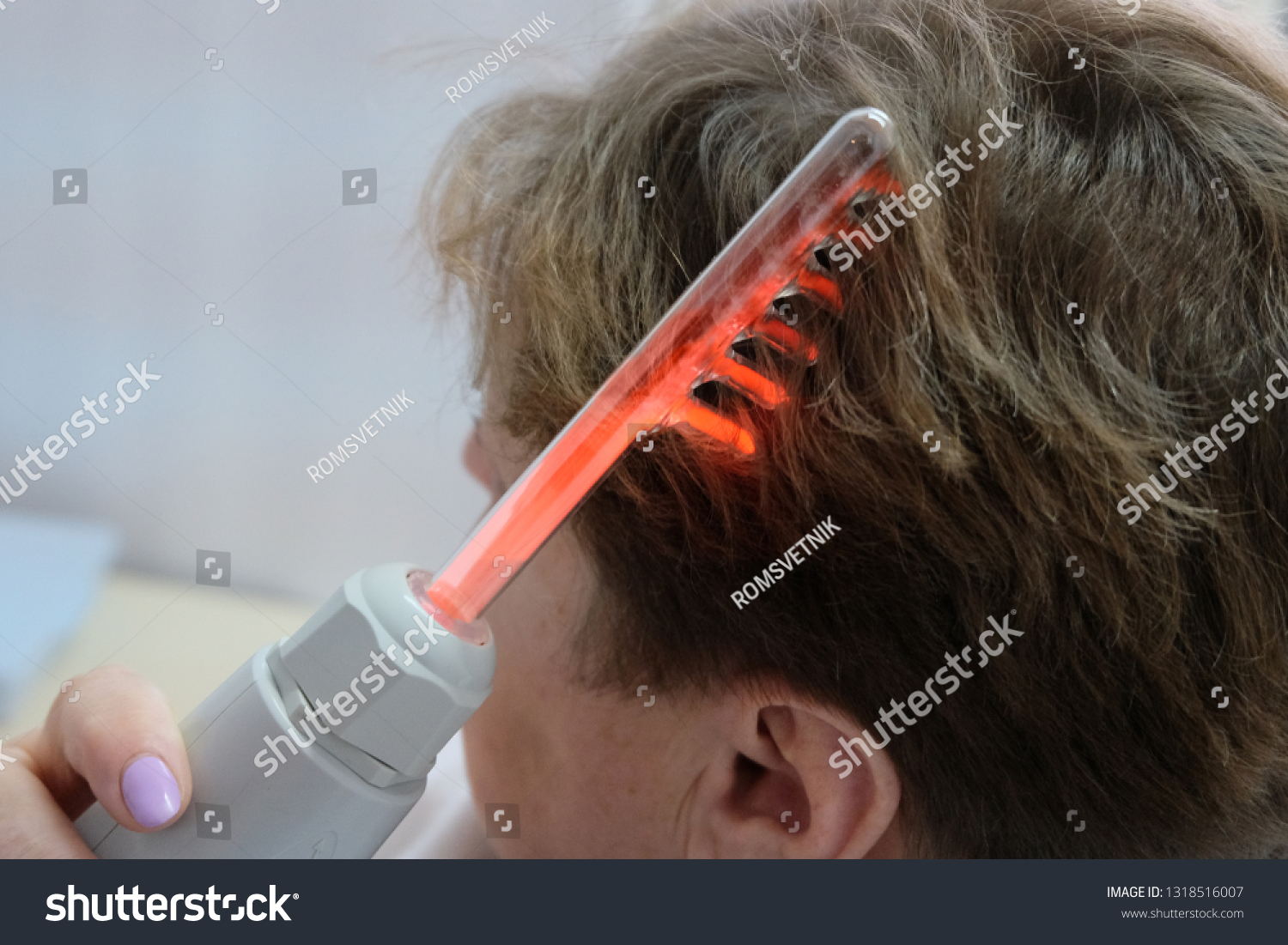 Woman combing hair with electric comb. d'Arsonval is a device for the physiotherapeutic effect on the tissues of the human body with a high-frequency, high-voltage and low-current impulse quick #1318516007