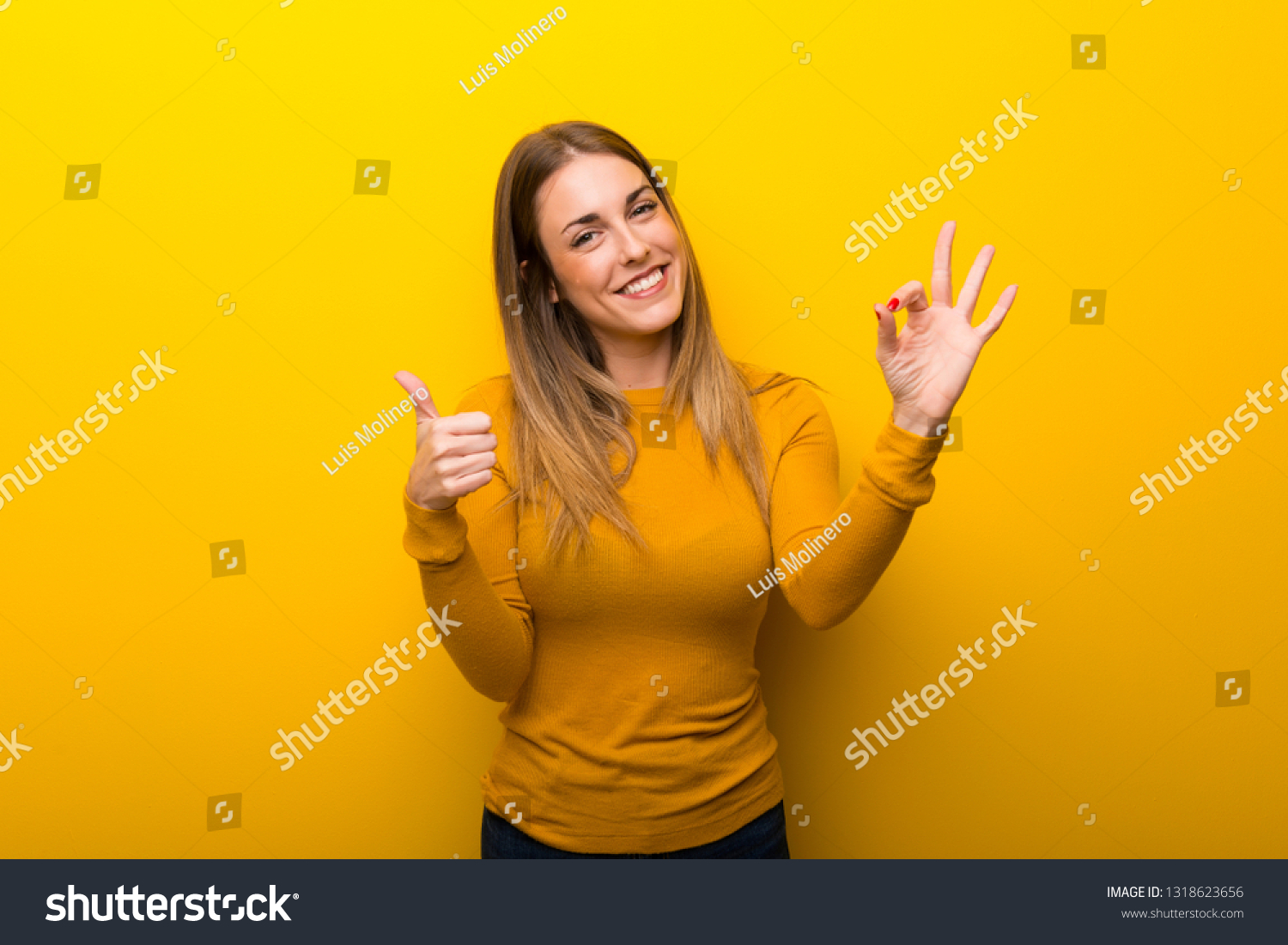 Young woman on yellow background showing ok sign with and giving a thumb up gesture #1318623656